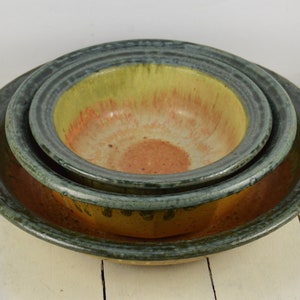 May include: Set of three ceramic bowls with a green, yellow, and orange glaze. The bowls are nested inside each other.