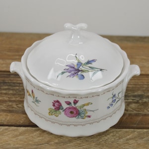 May include: White porcelain soup tureen with a lid, featuring a floral design with pink, purple, and blue flowers. The tureen has two handles and a scalloped edge.
