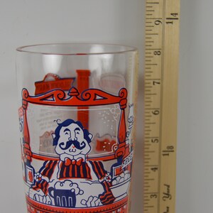 May include: A clear glass with a red, white, and blue illustration of a man with a mustache sitting at a bar with a beer mug. The glass is 7 inches tall.