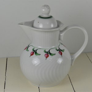 May include: White ceramic coffee pot with a green and pink floral design. The pot has a lid with a small knob on top.