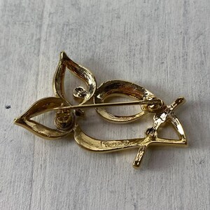 Op de afbeelding: Een goudkleurige broche met een bloemmotief. De broche heeft drie bloemblaadjes en een gebogen, langwerpige vorm. De speld is zichtbaar aan de achterkant.