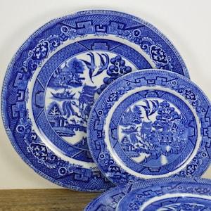 May include: Three blue and white porcelain plates with a traditional willow pattern. The plates are nested together, with the largest plate in the back and the smallest plate in the front.