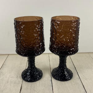 May include: Two brown textured glass goblets with black bases and stems. The goblets have a unique, organic texture on the bowl and stem, creating a vintage aesthetic. The glasses are suitable for serving beverages.