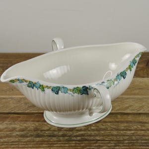 May include: White porcelain gravy boat with green and yellow ivy design. The boat has two handles and a fluted base.