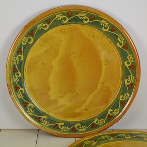 May include: A yellow ceramic plate with a green and red floral border. The plate has a rustic, hand-painted look.