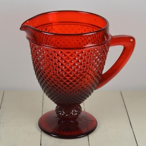 May include: A red glass pitcher with a diamond pattern and a footed base.
