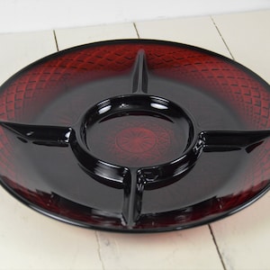May include: A round, divided serving platter with a deep red, textured rim and a black center. The platter has four sections, including a central circular compartment. The rim features a diamond pattern.