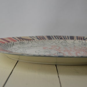 May include: A white oval serving platter with a black and red patterned rim. The center of the platter features a floral design in black and pink.
