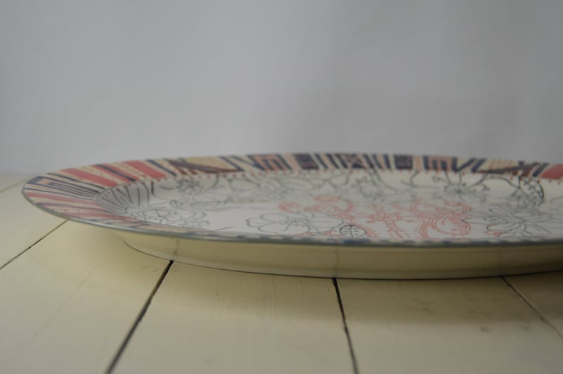 May include: A white oval serving platter with a black and red patterned rim. The center of the platter features a floral design in black and pink.
