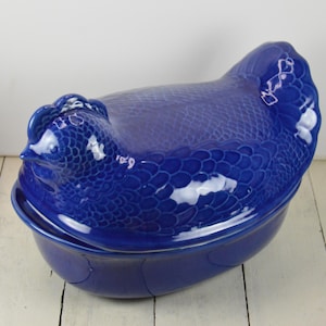 May include: A blue ceramic chicken-shaped casserole dish with a textured surface. The dish has a lid that fits snugly on top.