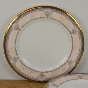 May include: A set of two white ceramic dinner plates with a gold rim and a pink and gray marble design. The plates feature a decorative shell design.