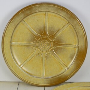 May include: A large, round, yellow ceramic plate with a wheel design. The plate has a raised rim and a center design that resembles a sun.