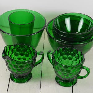 May include: Set of green glass bowls and creamer and sugar set. The bowls are stacked and the creamer and sugar set have a textured, bubbled design.