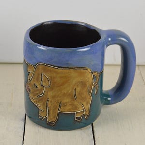 May include: A blue and green ceramic coffee mug with a brown pig illustration. The pig is facing left and has a pink snout.