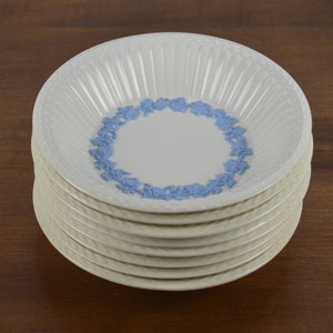 May include: A stack of ten white ceramic bowls with a blue floral design around the rim. The bowls have a fluted design on the inside.