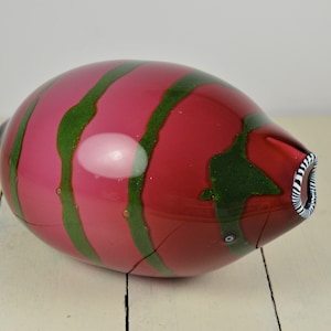 May include: A pink and green glass vase with a striped pattern. The vase has a rounded shape and a small opening at the top.