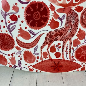 Op de afbeelding: Een witte keramische schaal met een rood en bordeaux bloemen- en dierenontwerp. Het ontwerp omvat een gestileerd hert met gedetailleerde patronen, bloemen en bladeren. De schaal heeft een afgeronde vorm.
