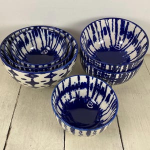 May include: A set of ceramic bowls in varying sizes. The bowls feature a white and navy blue tie-dye pattern. The bowls are arranged on a white wooden surface. The bowls have a glossy finish and a simple, modern design.