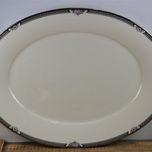 May include: An oval serving platter with a cream-colored background and a gold and black border. The border is decorated with a floral pattern in shades of pink, blue, and green.