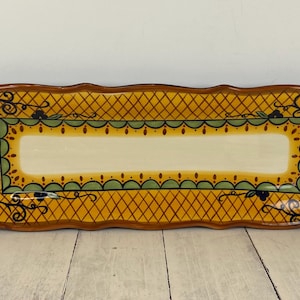 May include: Rectangular ceramic serving platter with a yellow diamond pattern and a cream-colored center. The edges are brown with decorative floral and paisley designs in green, red, and blue.