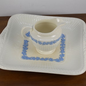 May include: A white ceramic creamer with a blue floral design sits on a white ceramic square serving tray with a blue floral border.