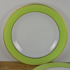 May include: A white ceramic plate with a green and gold rim. The plate is round and has a smooth surface.