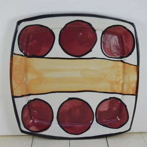 May include: A white ceramic serving platter with a black rim and a yellow stripe. The platter is decorated with six red circles.
