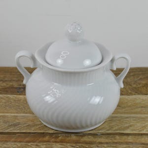 May include: White porcelain sugar bowl with a lid and two handles. The bowl has a swirl design.