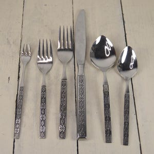 May include: Set of six silver-toned flatware with floral designs on the handles. The set includes a knife, fork, and spoon.