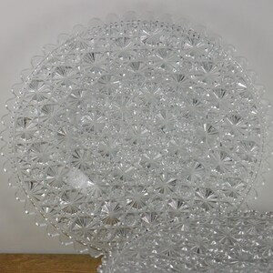 May include: Two clear glass plates with a decorative, raised, floral pattern. The plates are stacked on top of each other.