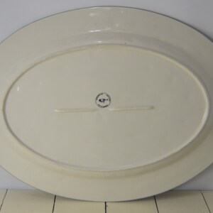 May include: White oval serving platter with a blue rim. The platter has a small black and white logo on the bottom.