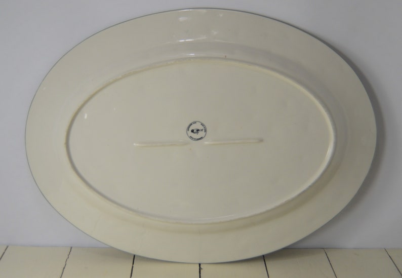 May include: White oval serving platter with a blue rim. The platter has a small black and white logo on the bottom.