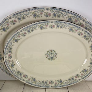 May include: Two oval serving platters with a cream-colored base. The platters feature a blue and pink floral design around the edges and a silver trim. A smaller floral design is in the center of the platters.