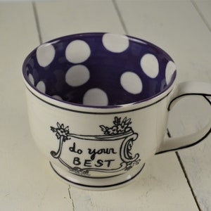 May include: White ceramic mug with a purple interior featuring white polka dots. The mug has a black handle and a decorative black border. The words "do your BEST" are written on the front of the mug in black script.