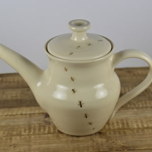 May include: A white ceramic teapot with a lid, featuring a design of small brown ants crawling on the surface.