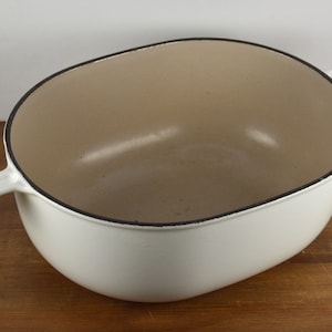 May include: White oval cast iron Dutch oven with two handles. The interior is a light brown color.