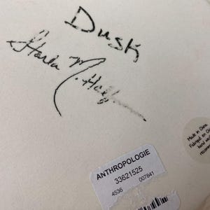 May include: Close-up of a white ceramic plate with black handwritten text that reads "Dusk" and a signature. A sticker with the word "ANTHROPOLOGIE" and other details is visible.