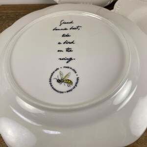 May include: White ceramic plate with a scalloped edge. The plate features a black inscription that reads "Freed Lonnie beat, like a bird on the wing." A yellow and black bee illustration is also present, along with text indicating it is microwave and dishwasher safe.