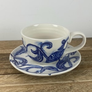 Puede incluir: Juego de taza y platillo de t&eacute; de cer&aacute;mica blanca con dise&ntilde;os florales abstractos azules. La taza de t&eacute; tiene un asa y el platillo es redondo. Los dise&ntilde;os azules est&aacute;n pintados en el exterior de la taza y el platillo.