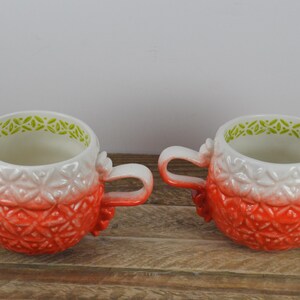 May include: Two red and white ceramic mugs with green trim and a textured design. The mugs have a gradient effect from white to red.