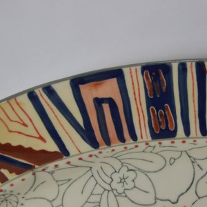 May include: A ceramic plate with a white background and a colorful geometric design around the rim. The center of the plate features a floral pattern in black and white.