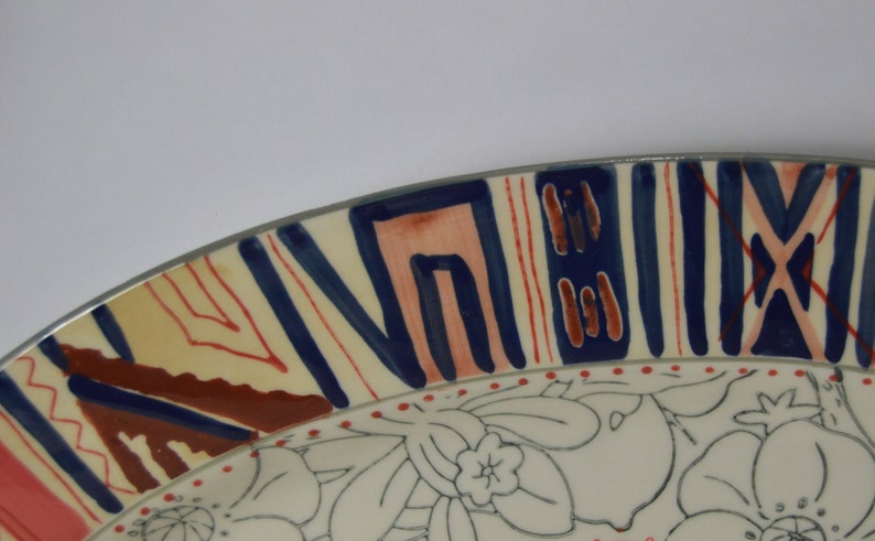 May include: A ceramic plate with a white background and a colorful geometric design around the rim. The center of the plate features a floral pattern in black and white.