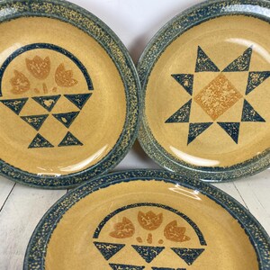 May include: Set of three ceramic plates with a yellow center and a blue rim. Each plate features a unique design: a basket of flowers, a starburst, and a floral pattern. The plates are suitable for serving food.