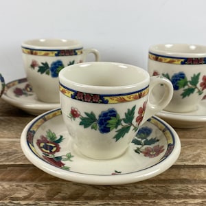 May include: Set of four cream-colored teacups and saucers. Each cup and saucer features a floral design with blue, red, and green accents. The rims are decorated with a yellow and blue border.