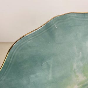 May include: A section of a decorative plate with a scalloped edge and a gold rim. The plate has a light teal background with a blue and yellow floral design. The plate is likely made of ceramic.