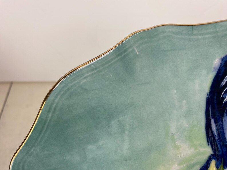 May include: A section of a decorative plate with a scalloped edge and a gold rim. The plate has a light teal background with a blue and yellow floral design. The plate is likely made of ceramic.