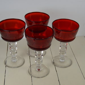 May include: Set of four red glass stemmed wine glasses with clear glass stems and bases.