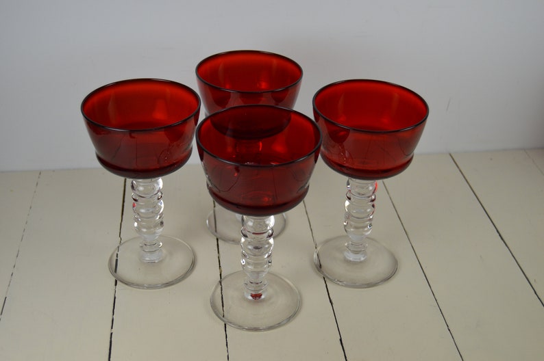 May include: Set of four red glass stemmed wine glasses with clear glass stems and bases.