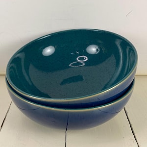 May include: Two stacked round ceramic bowls with a glossy finish. The top bowl is a deep teal color with subtle dark speckles, while the bottom bowl is a solid dark navy blue. Both bowls feature a thin, light-colored rim along the top edge.