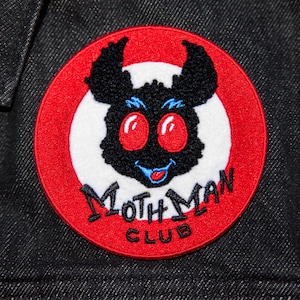 May include: Embroidered patch featuring a cartoon Mothman character with red eyes, a blue smile, and black fur, set against a white circle and a red border. The text "Mothman Club" is arched below the image.